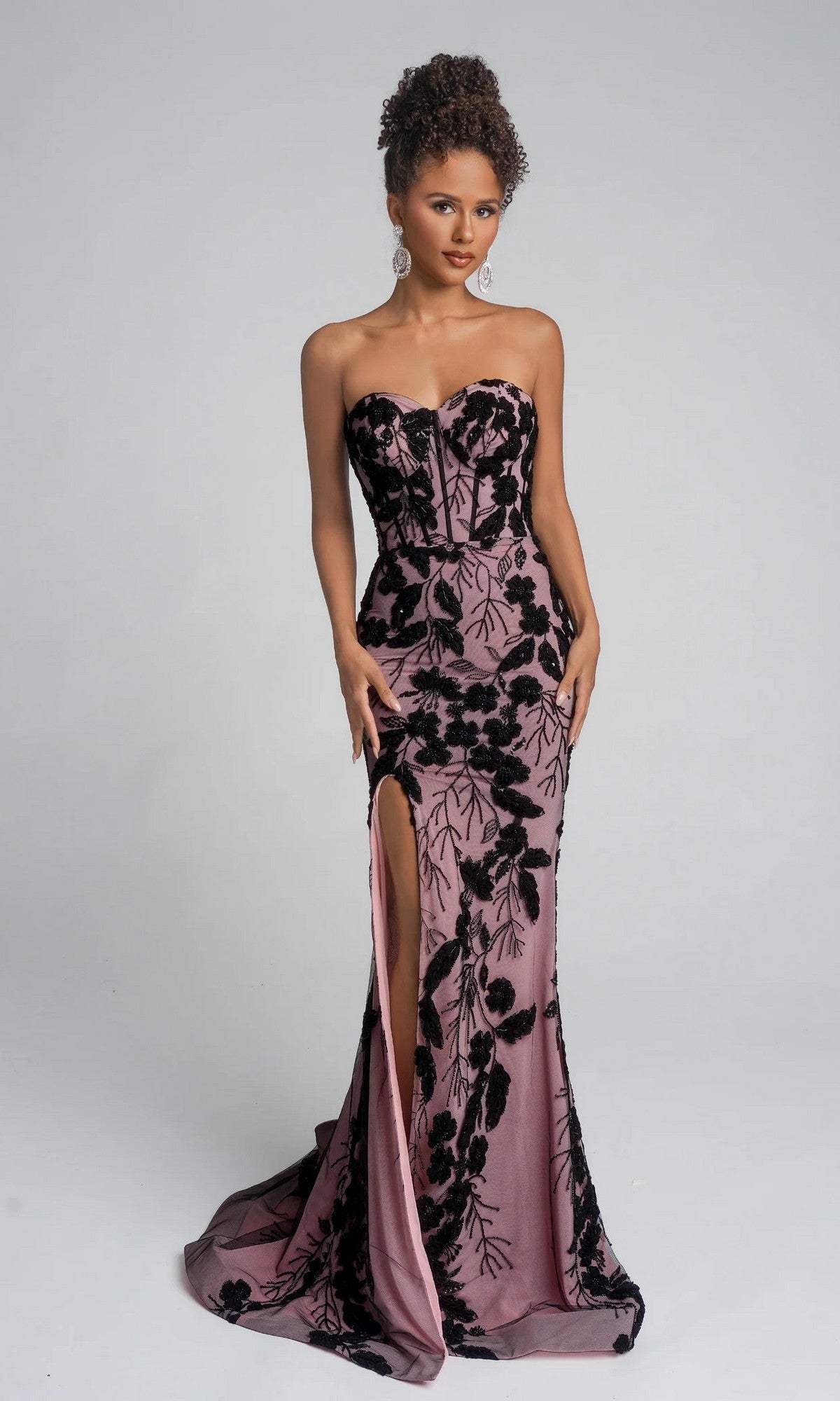 A woman poses against a light gray background wearing the Portia and Scarlett PS26074 long formal dress in black/nude, featuring a strapless sweetheart neckline, black floral patterns, and a thigh-high leg slit.